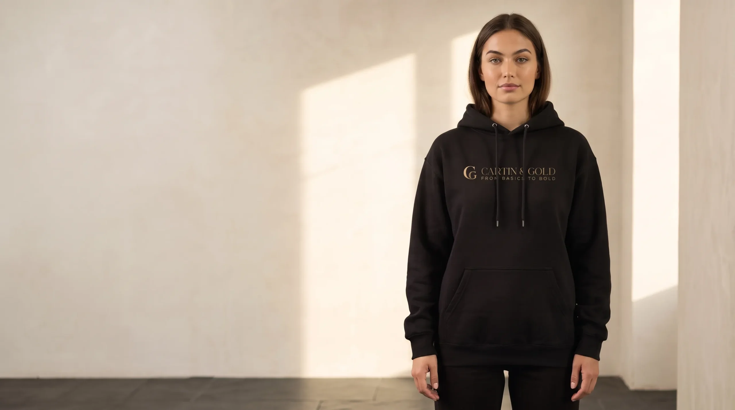 Model wearing the black Cartin & Gold hoodie in a warm cream studio